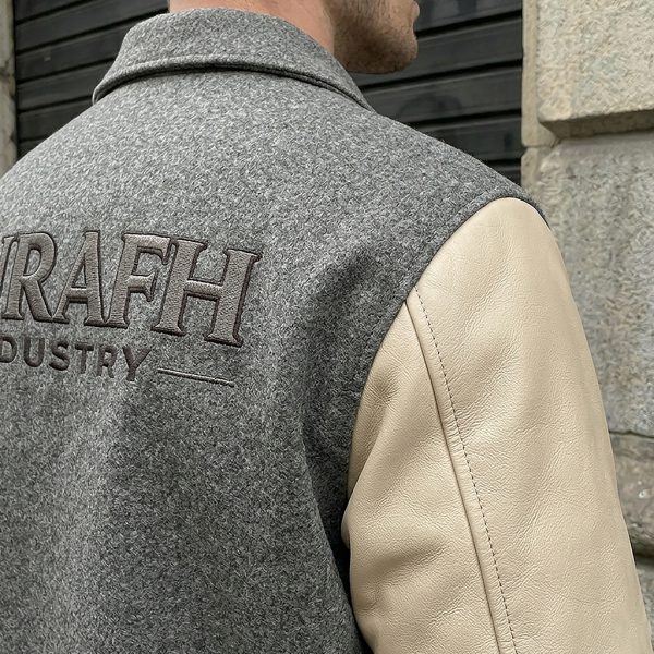 Macro factory studio shot focusing on the high-definition embroidery stitch quality on the grey wool body beside the clean top-grain cream leather sleeve shoulder seam.
