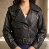 Close-up cropped front view of a women's black leather biker jacket showing the premium asymmetric zipper details, metal snap buttons, a structured pocket flap, and a buckled waist belt.