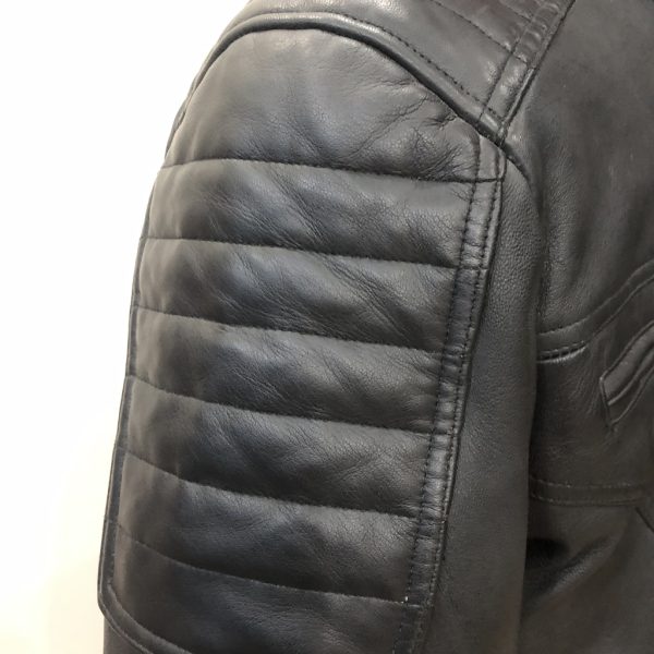 Macro shot of an OEM black leather jacket highlighting the precise industrial stitching on the horizontal quilted padding across the shoulder panel.