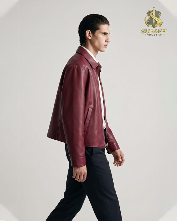 Side profile perspective of a model walking while wearing a private label deep wine red leather jacket highlighting the clean drape, welt pockets, and drop shoulder paneling.