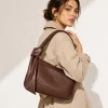 Woman holding brown crocodile-embossed leather shoulder bag with knot handle detail