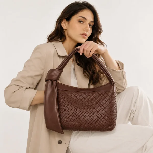 Woman wearing brown crocodile-embossed leather shoulder bag with knot handle, side view